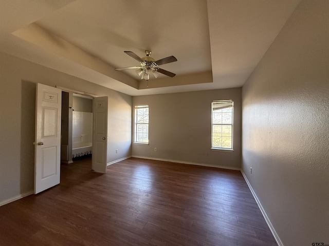 spare room with a ceiling fan, baseboards, a raised ceiling, and dark wood-style flooring