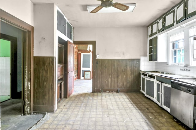 kitchen with a sink, wainscoting, wooden walls, a ceiling fan, and dishwasher