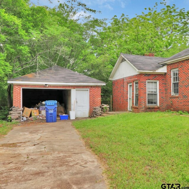 exterior space featuring a detached garage, driveway, brick siding, an outdoor structure, and a yard