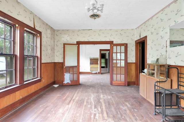 unfurnished dining area featuring wainscoting, wood walls, hardwood / wood-style flooring, and french doors