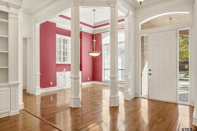 foyer with hardwood / wood-style flooring, a towering ceiling, crown molding, and decorative columns