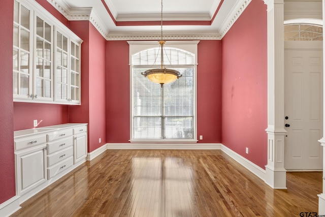 unfurnished dining area with decorative columns, a tray ceiling, hardwood / wood-style flooring, and ornamental molding