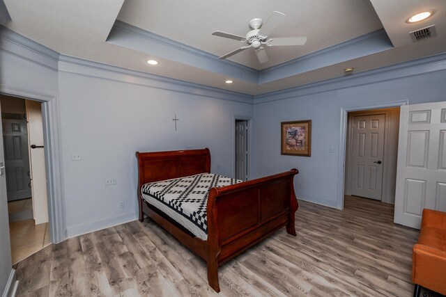 bedroom featuring light hardwood / wood-style flooring, a tray ceiling, and ornamental molding