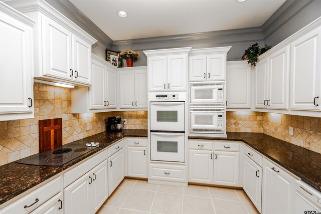 kitchen with white cabinets, light tile patterned floors, dark stone counters, and white appliances