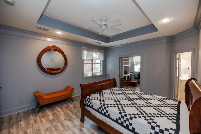 bedroom with a tray ceiling, light wood-type flooring, crown molding, and multiple windows