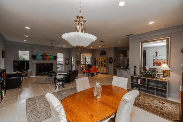 tiled dining area with ceiling fan, crown molding, and a fireplace