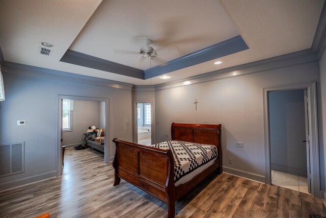 bedroom featuring a raised ceiling, wood-type flooring, and multiple windows