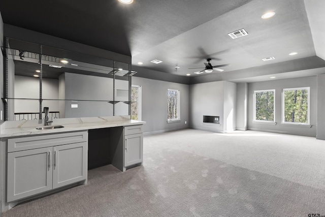 interior space with ceiling fan, sink, light carpet, and light stone counters