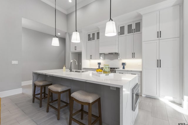 kitchen featuring stainless steel microwave, decorative light fixtures, an island with sink, and white cabinets