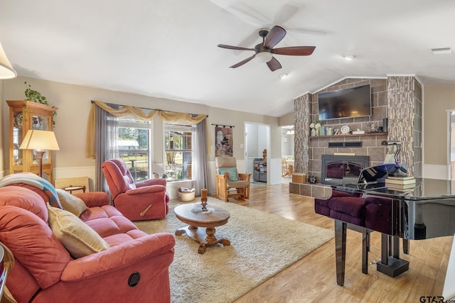 living room with hardwood / wood-style floors, ceiling fan, a stone fireplace, and lofted ceiling