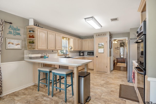 kitchen featuring kitchen peninsula, sink, oven, a kitchen breakfast bar, and light brown cabinets