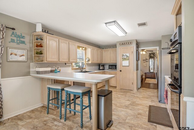 kitchen featuring kitchen peninsula, sink, oven, a kitchen breakfast bar, and light brown cabinets