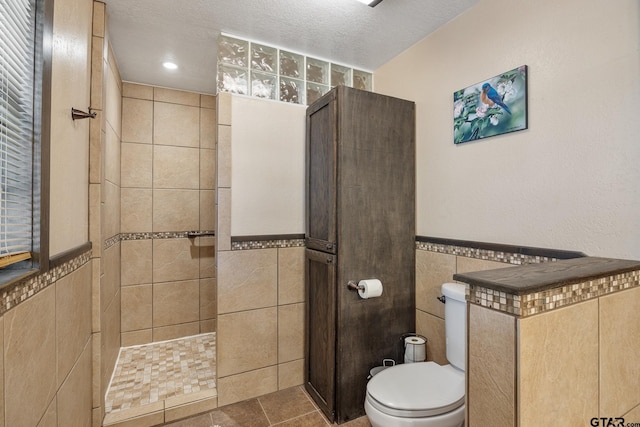 bathroom featuring tile walls, tile patterned floors, tiled shower, a textured ceiling, and toilet