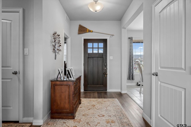 foyer with baseboards, visible vents, and dark wood-style flooring