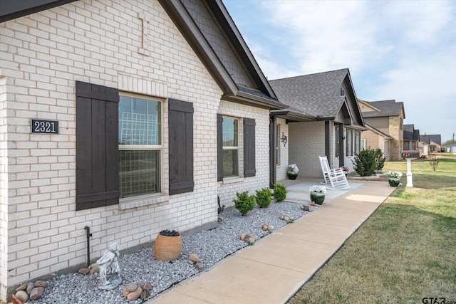 view of side of property featuring a lawn, brick siding, and a shingled roof