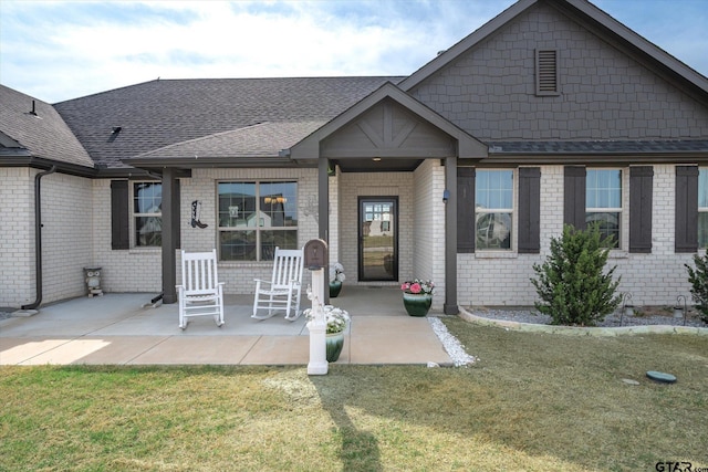 view of front of home featuring a front lawn, a patio, brick siding, and roof with shingles