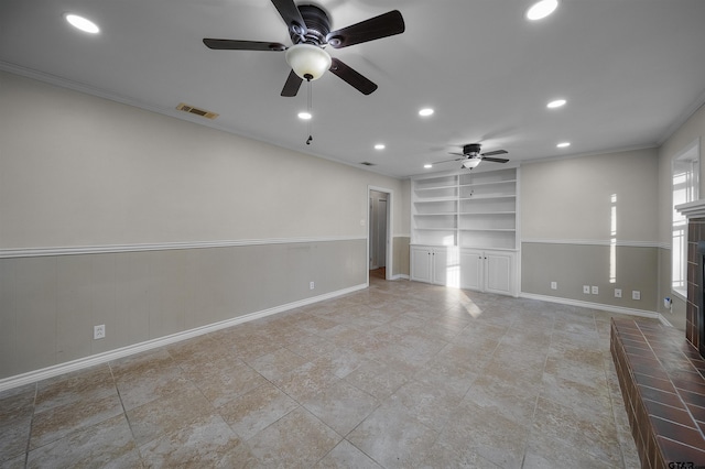 empty room with ceiling fan, built in shelves, crown molding, and a fireplace