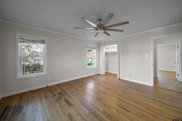 unfurnished bedroom featuring ceiling fan, wood-type flooring, a spacious closet, and crown molding