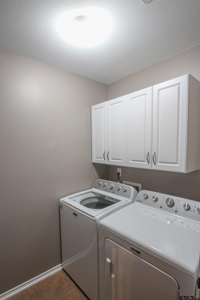laundry area featuring washer and clothes dryer, a textured ceiling, tile patterned floors, cabinet space, and baseboards