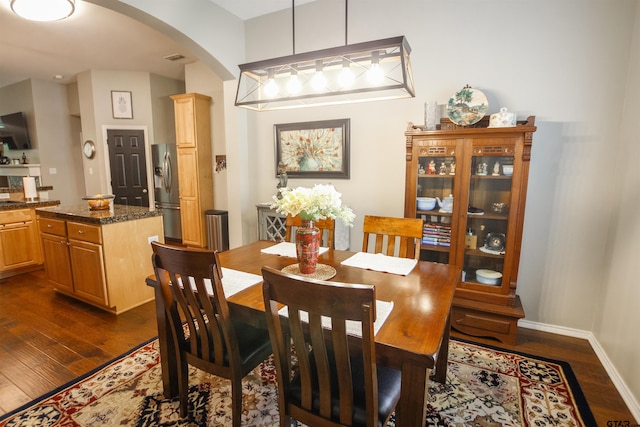 dining space featuring arched walkways, dark wood-type flooring, and baseboards