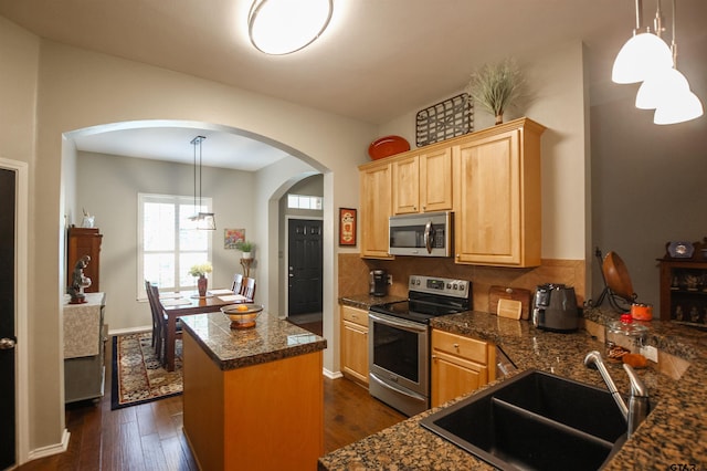 kitchen with light brown cabinetry, backsplash, a sink, arched walkways, and appliances with stainless steel finishes