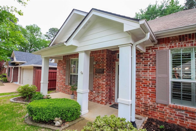 view of exterior entry featuring roof with shingles, driveway, a porch, brick siding, and a garage