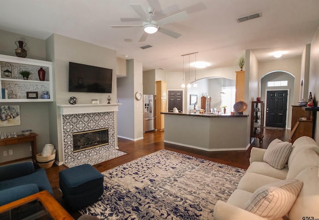 living room featuring a fireplace, visible vents, a ceiling fan, and dark wood-style floors