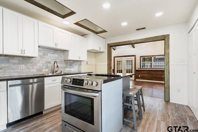 kitchen with sink, appliances with stainless steel finishes, a kitchen breakfast bar, white cabinets, and french doors