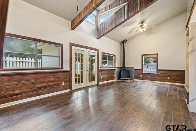 unfurnished living room with high vaulted ceiling, wooden walls, a wood stove, dark hardwood / wood-style flooring, and french doors