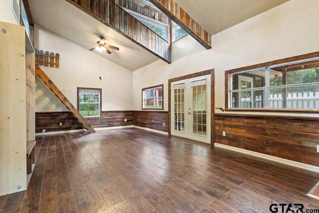 unfurnished living room with high vaulted ceiling, wood walls, dark hardwood / wood-style flooring, ceiling fan, and french doors