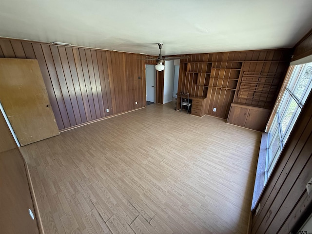 unfurnished living room with a ceiling fan, light wood-type flooring, and wood walls