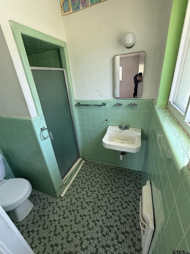 bathroom with tile walls, toilet, a stall shower, and a sink