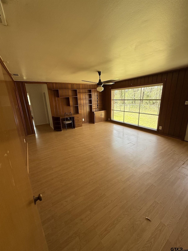 unfurnished living room featuring a ceiling fan, visible vents, light wood finished floors, wood walls, and a textured ceiling