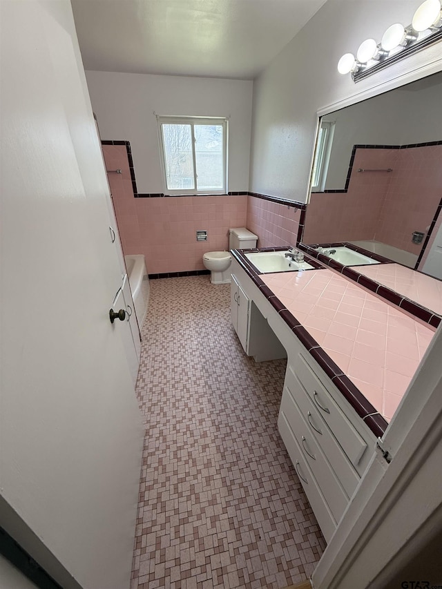 full bathroom featuring toilet, vanity, tile walls, wainscoting, and shower / bathtub combination