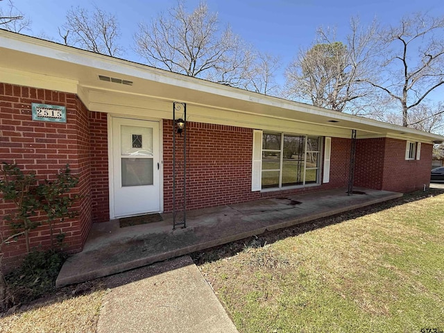 view of exterior entry featuring brick siding and a porch