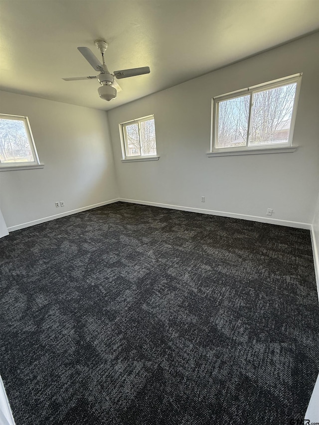 empty room with baseboards, dark colored carpet, and ceiling fan