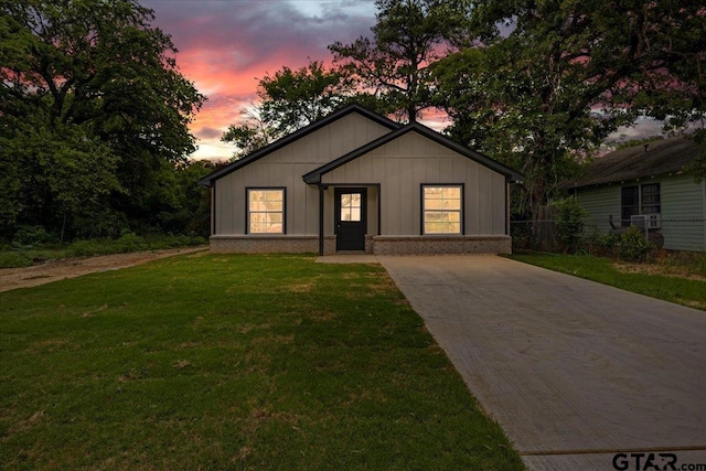 bungalow-style house with a front lawn, fence, brick siding, board and batten siding, and driveway