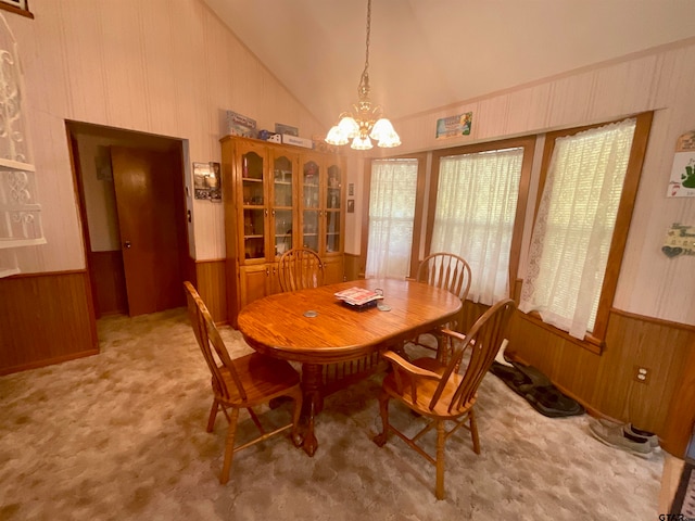 dining space with high vaulted ceiling, a chandelier, wooden walls, and light carpet