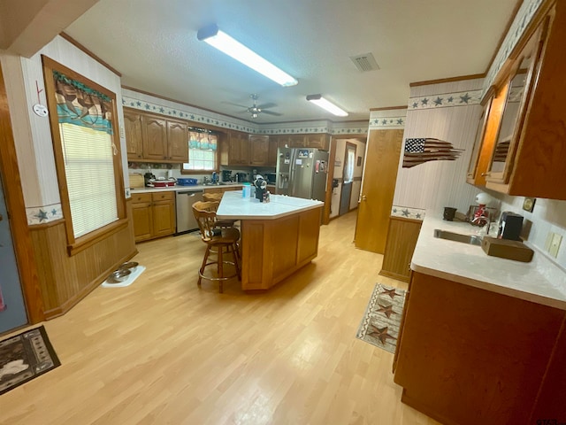 kitchen featuring light hardwood / wood-style floors, appliances with stainless steel finishes, ceiling fan, a breakfast bar area, and a kitchen island with sink