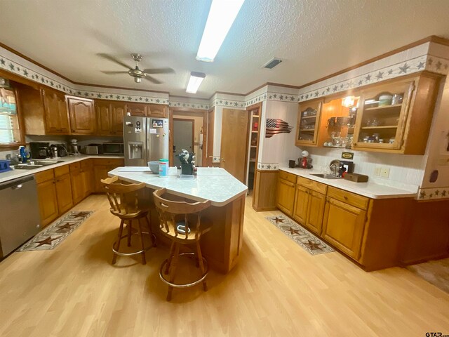 kitchen featuring stainless steel appliances, a kitchen island, light wood-type flooring, a textured ceiling, and a breakfast bar