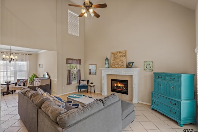 living room with ceiling fan with notable chandelier, light tile patterned flooring, a tile fireplace, and a high ceiling