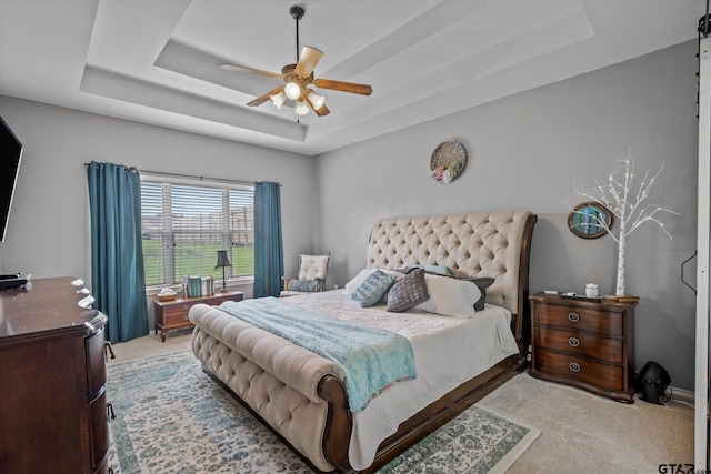 bedroom with a tray ceiling, ceiling fan, and light carpet