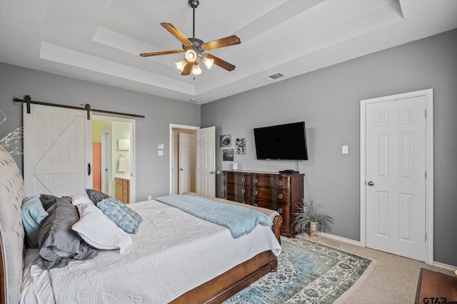 carpeted bedroom with a barn door, ensuite bath, a raised ceiling, and ceiling fan