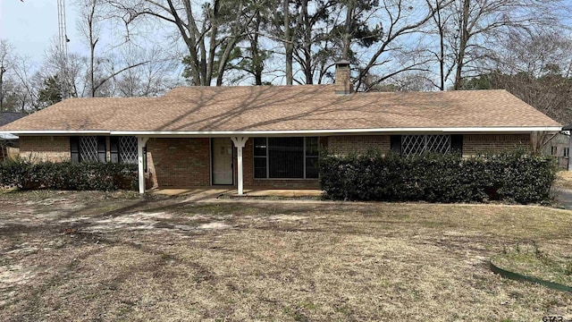 view of front of home featuring a shingled roof, brick siding, and a chimney