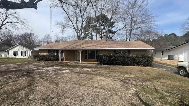 ranch-style home featuring central air condition unit, covered porch, a chimney, and brick siding