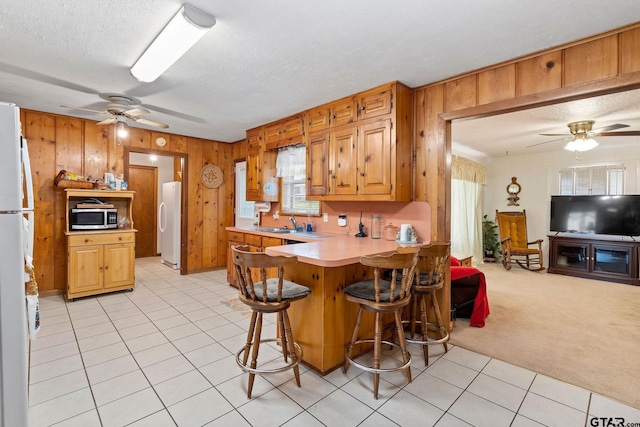 kitchen featuring light colored carpet, a breakfast bar, kitchen peninsula, and white fridge