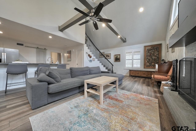 living room with a fireplace with raised hearth, stairway, beamed ceiling, wood finished floors, and high vaulted ceiling