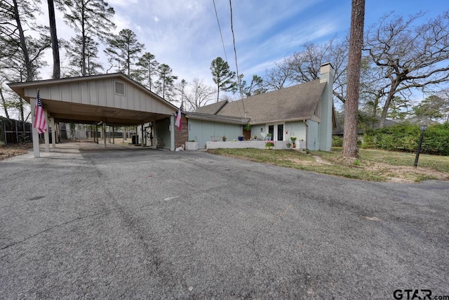 view of front facade featuring a carport, driveway, a chimney, and roof with shingles