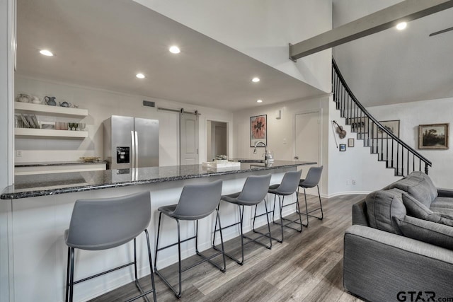 kitchen with dark stone countertops, a barn door, wood finished floors, and stainless steel refrigerator with ice dispenser