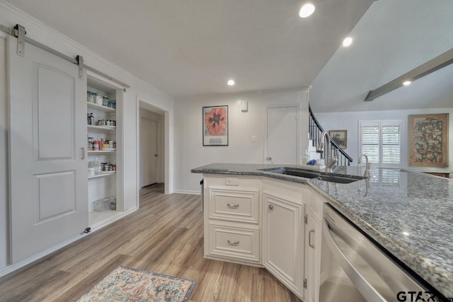 kitchen featuring stone counters, a sink, light wood-style floors, dishwasher, and a barn door